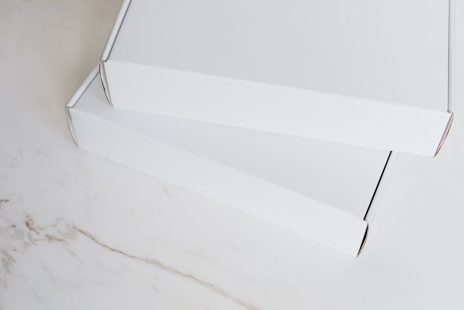 From above of pair of closed white cardboard boxes for postal or courier delivery arranged on white marble tabletop for sending preparation